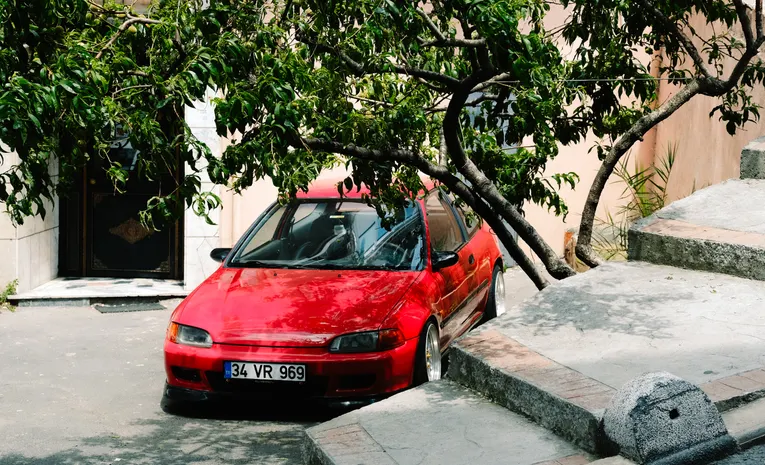 Red Honda Civic hatchback parked under a tree showing body style