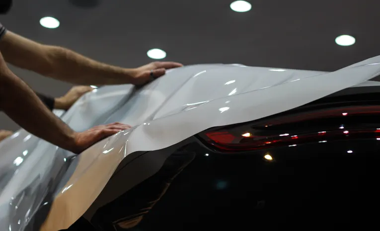 Professional applying a vinyl wrap to a car in a UK workshop showing car wrap cost process