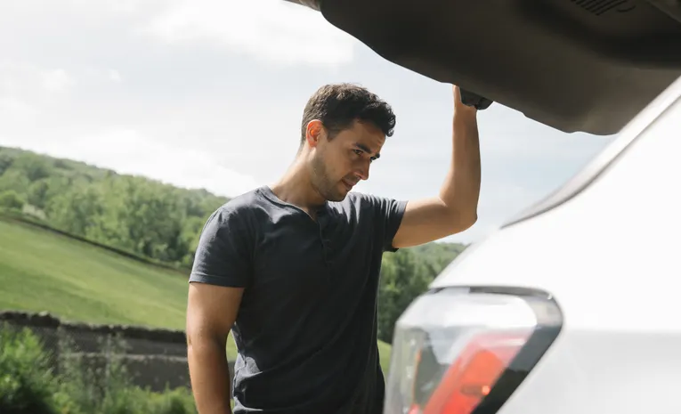 Man checking the open boot space of a car parked outdoors