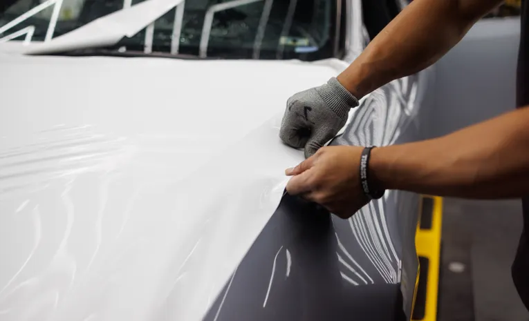 Close-up of hands applying a vinyl wrap film to a car panel